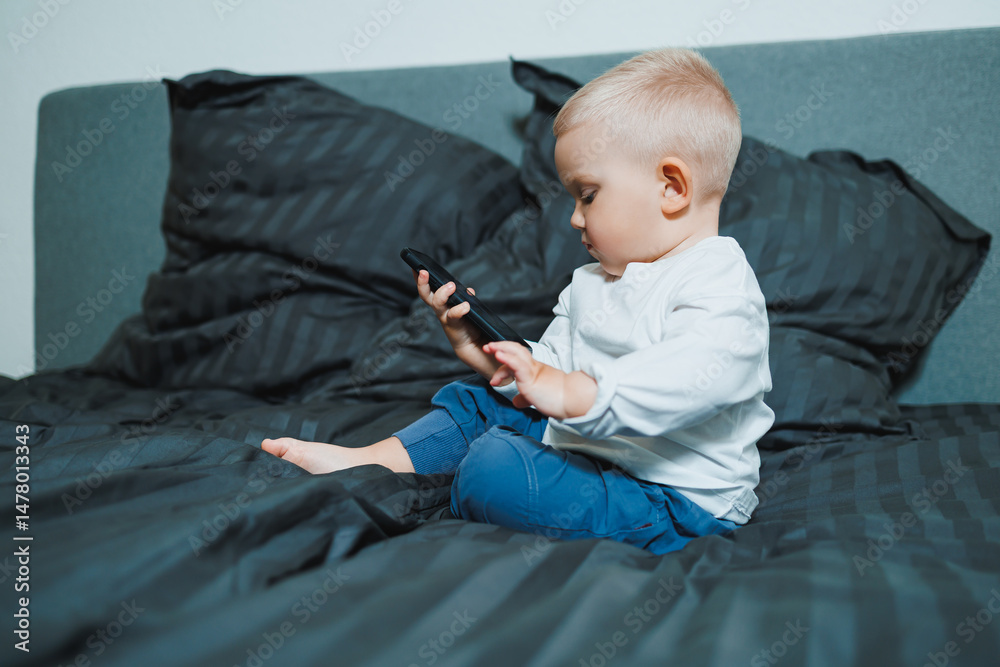 A toddler is comfortably engaged with a smartphone while nestled in a cozy bed, showcasing a blend of innocence, curiosity, and the interaction between childhood and modern technology