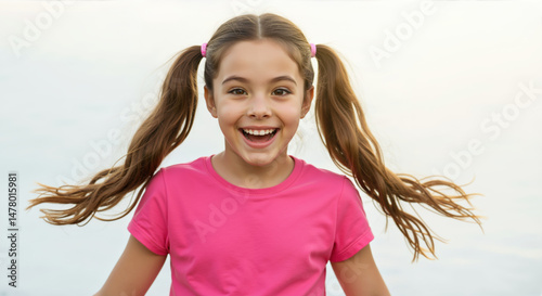 Laughing girl with pigtails in pink t-shirt against white sky background with flying hair. Joyful summer portrait for children's active lifestyle campaigns