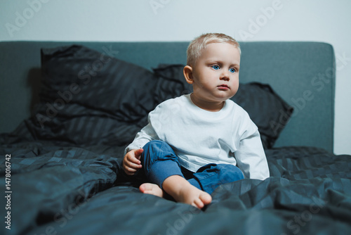 Obraz na płótnie A Thoughtful Toddler is Sitting on a Bed Surrounded by Cozy Cushions in a Modern Bedroom Setting that exudes warmth and comfort, providing an inviting atmosphere for relaxation and play w salonie
