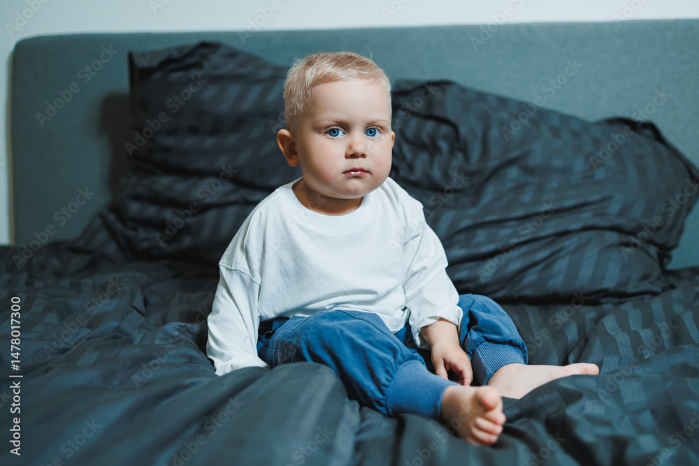 An adorable toddler is sitting on a bed, showcasing a curious expression that captures the enchanting essence of childhood in a cozy bedroom setting filled with warmth and comfort