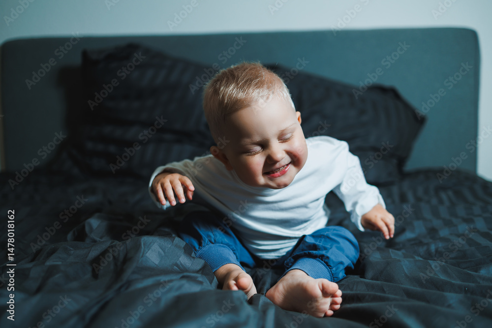 An adorable baby radiating a bright smile is sitting comfortably on a cozy bed, illuminated by soft, gentle lighting that enhances the scenes warmth and charm, showcasing pure innocence and joy