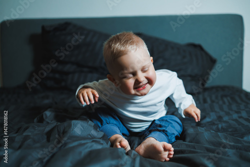 Obraz na płótnie An adorable baby radiating a bright smile is sitting comfortably on a cozy bed, illuminated by soft, gentle lighting that enhances the scenes warmth and charm, showcasing pure innocence and joy w salonie