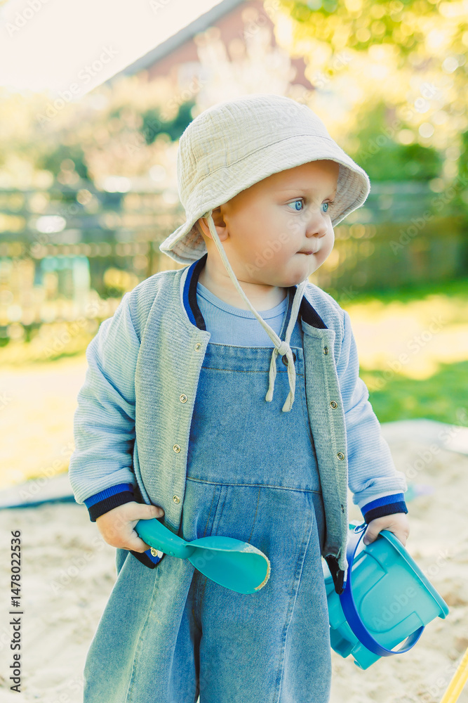 A cute toddler joyfully playing in a sandbox filled with colorful toys on a warm, sunny day, enjoying the bright sunshine while exploring their backyard and discovering new adventures
