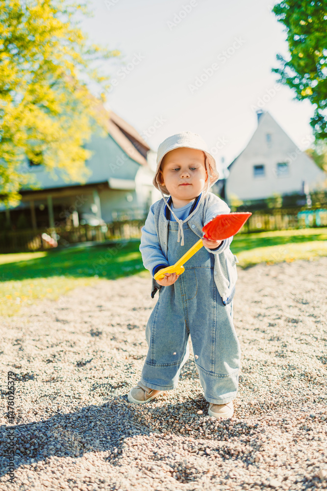 A cheerful and playful young toddler is having an enjoyable time playing outdoors with a bright and colorful shovel in a sunlit backyard, making the most of their childhood experiences