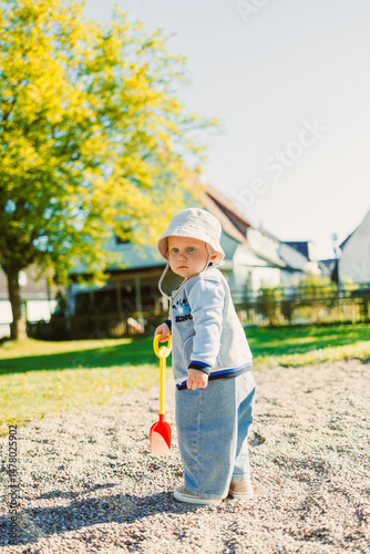Obraz na płótnie A joyful little toddler excitedly explores the sunny playground with a colorful shovel, fostering a sense of adventure and creativity for all the children and crafting delightful memories together w salonie