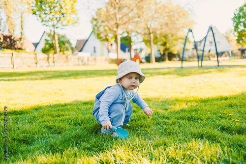 Obraz na płótnie A cheerful toddler plays joyfully in a sunny park, surrounded by greenery and blue sky, engaged in activities that reflect the innocence and bliss of childhood while exploring their world w salonie
