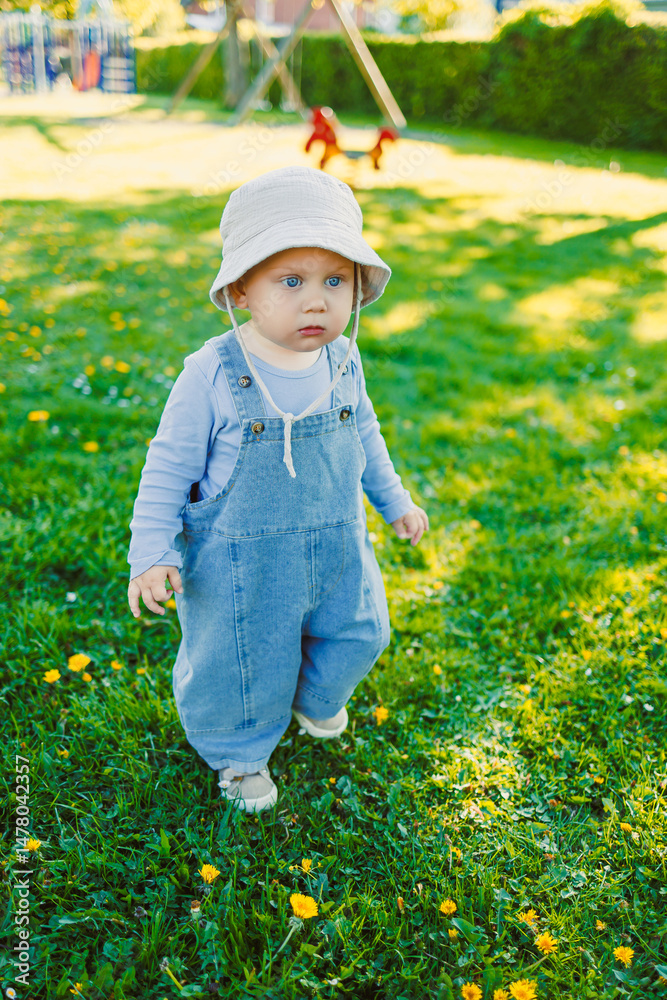 In a sunny park adorned with vibrant blooming flowers, an adorable baby dressed in cute overalls and an adorable hat joyfully plays, capturing the true essence of childhood innocence and carefree fun