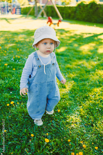 Obraz na płótnie In a sunny park adorned with vibrant blooming flowers, an adorable baby dressed in cute overalls and an adorable hat joyfully plays, capturing the true essence of childhood innocence and carefree fun w salonie