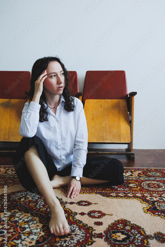 In a serene, minimalist indoor environment, a contemplative woman sits on a beautifully colorful rug, embodying a sense of calmness while deeply engaging in her thoughts and creative pursuits