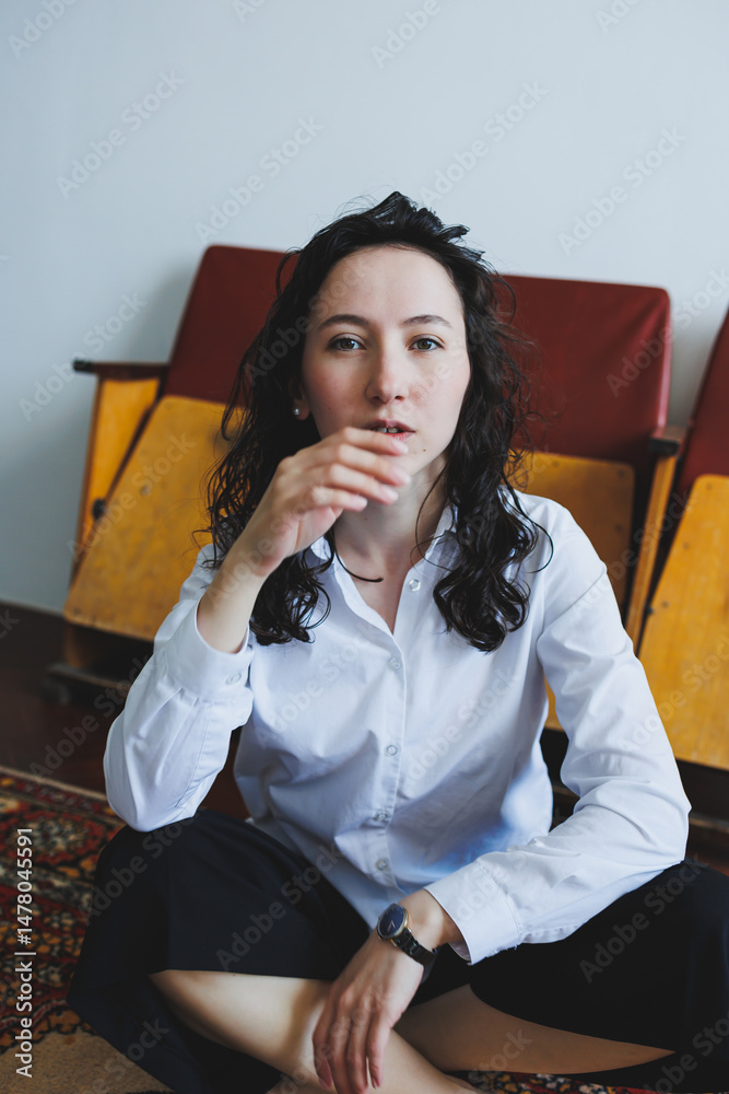 A Pensive Young Woman Dressed in Casual Attire is Sitting Comfortably in a Modern Living Space, Engaging in Deep Reflection Over Her Thoughts and Emotions, Indulging in a Moment of Introspection