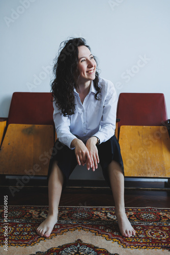 Obraz na płótnie A Joyful Portrait of a Young Woman in Casual Attire, Comfortably Sitting on Vintage Furniture, Radiating Positive Energy and Happiness, Captured in a Cozy Indoor Setting with Stylish Decor w salonie