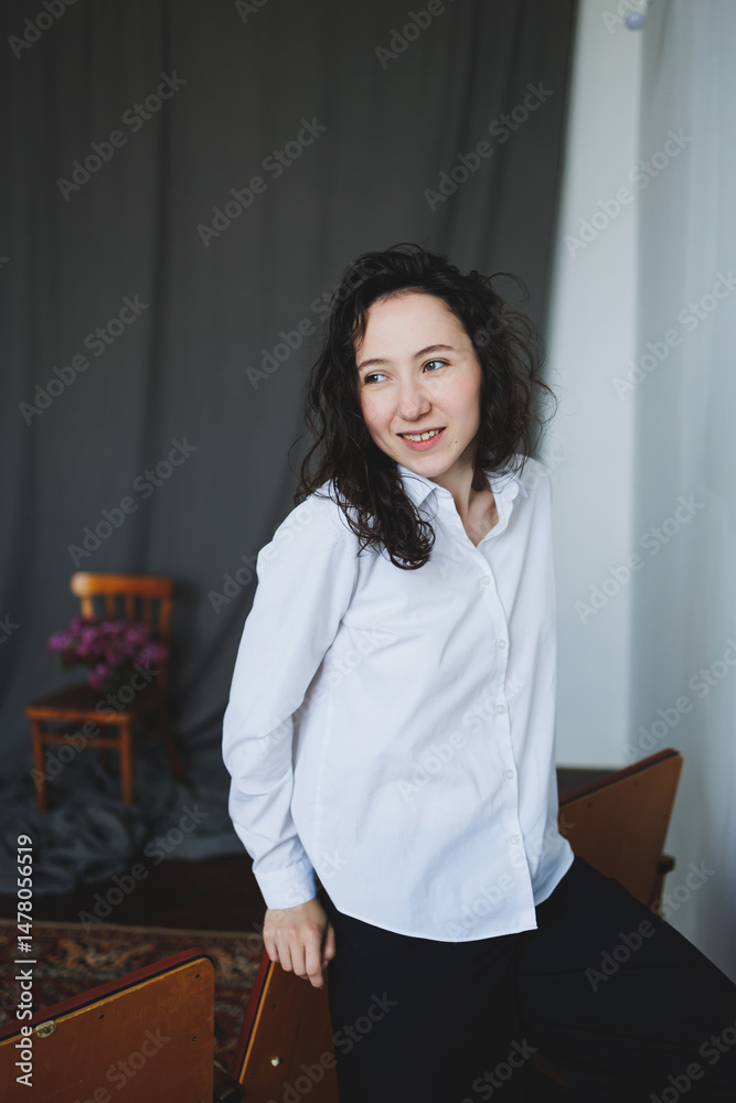 A stylish woman poses elegantly in a modern studio, showcasing her fashionable wardrobe. The artistic background enhances her vibrant lifestyle as she smiles casually in a comfortable chair