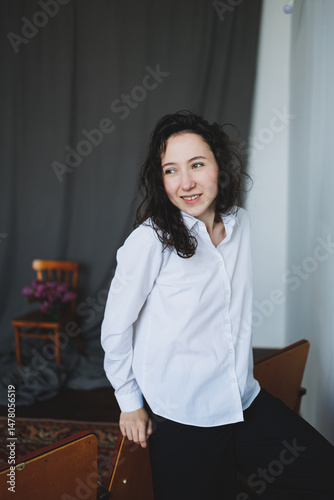 Obraz na płótnie A stylish woman poses elegantly in a modern studio, showcasing her fashionable wardrobe. The artistic background enhances her vibrant lifestyle as she smiles casually in a comfortable chair w salonie