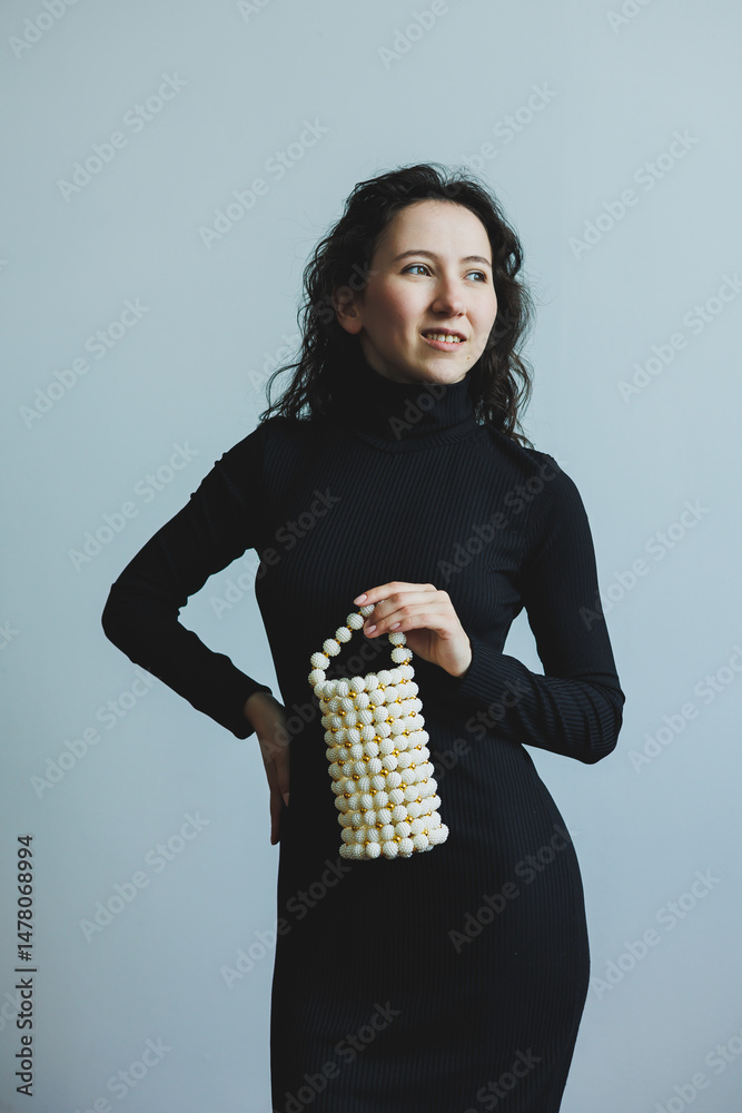 An Elegant Fashion Model is Posing Gracefully while Showcasing a Unique PearlStyle Handbag, all while wearing a Timeless Classic Black Dress that enhances her Charismatic Charm and Chic Style
