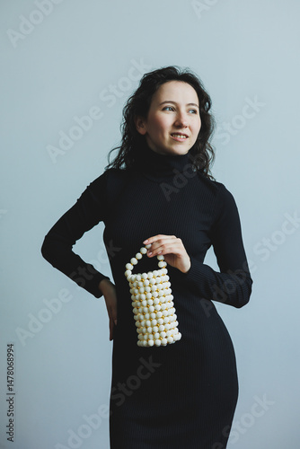 An Elegant Fashion Model is Posing Gracefully while Showcasing a Unique PearlStyle Handbag, all while wearing a Timeless Classic Black Dress that enhances her Charismatic Charm and Chic Style