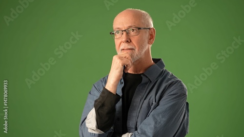 A senior man stands confidently against a solid green backdrop, showing joy with a bright smile and relaxed demeanor, captured during a portrait session.