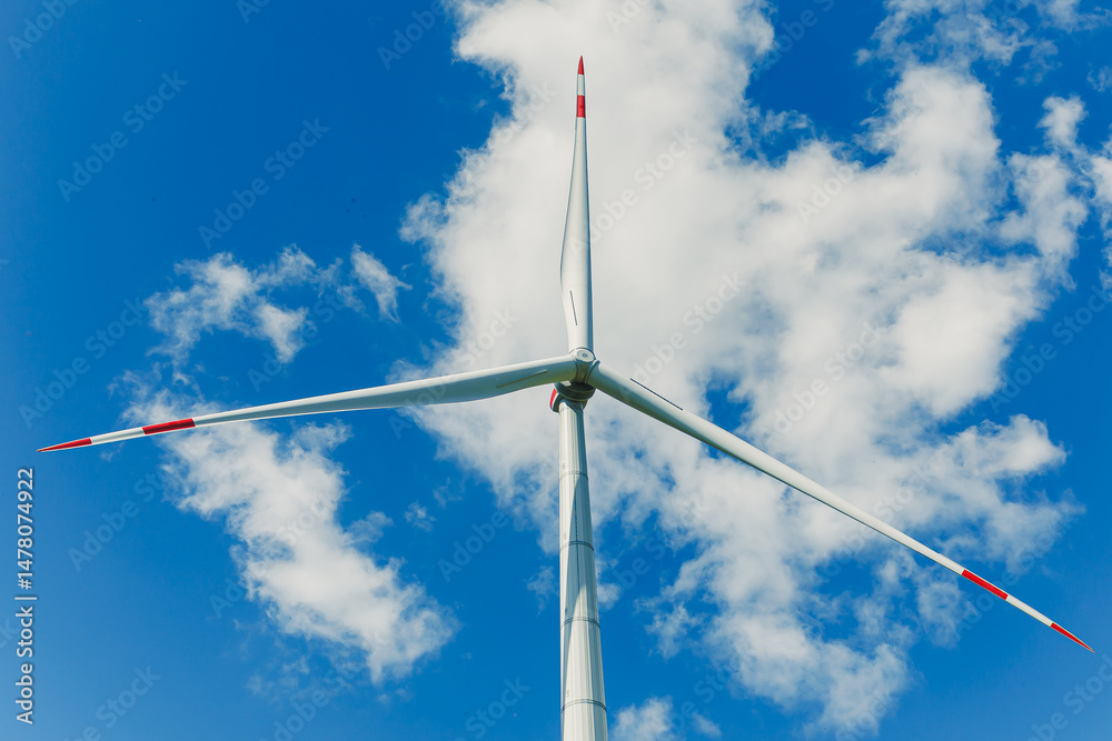 A tall wind turbine stands against a vibrant blue sky with fluffy white clouds, symbolizing the importance of renewable energy in promoting sustainability and supporting ecological health