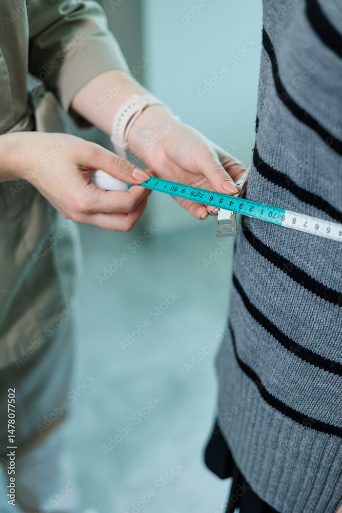 Measuring Waist Size for Tailoring A Professional Tailor is diligently Taking Measurements of a Clients Waist using a Measuring Tape inside a Creative Fashion Studio, ensuring the perfect fit