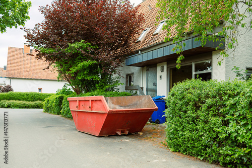 Large street garbage container. Metal red container for construction waste. Garbage container standing near the house during renovation.