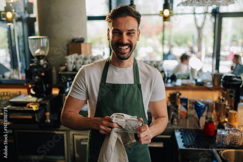 Smiling barista polishing glass in coffee shop