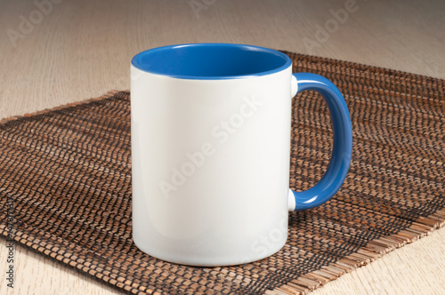 Two-tone 11oz mug on the straw mat on the table. Mug with bluehandle and inner part.