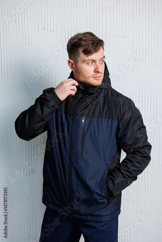 A very Stylish Man is adorned in a Navy and Black Windbreaker Jacket, confidently posing with great poise against a beautifully textured wall, exuding an undeniable sense of fashion and modernity