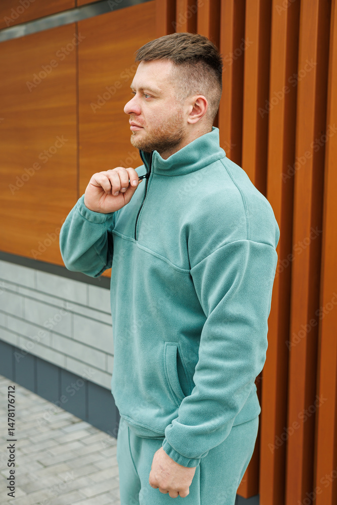 A fashionable and trendy man dressed in a cozy fleece jacket is confidently posing outdoors, set against a contemporary backdrop of warm wood and cool stone elements, creating a modern aesthetic