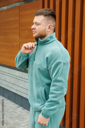 Obraz na płótnie A fashionable and trendy man dressed in a cozy fleece jacket is confidently posing outdoors, set against a contemporary backdrop of warm wood and cool stone elements, creating a modern aesthetic w salonie