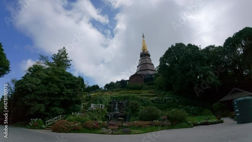 A panoramic view of the Phra Maha Chedi Tripob Trimongkol in Chiang Rai, Thailand, surrounded by lush gardens and a flowing waterfall.