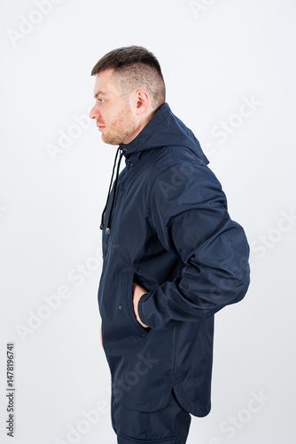 A young man is standing confidently in a dark blue jacket, striking a pose in profile. He is set against a simple, plain background that allows him to stand out and draw attention