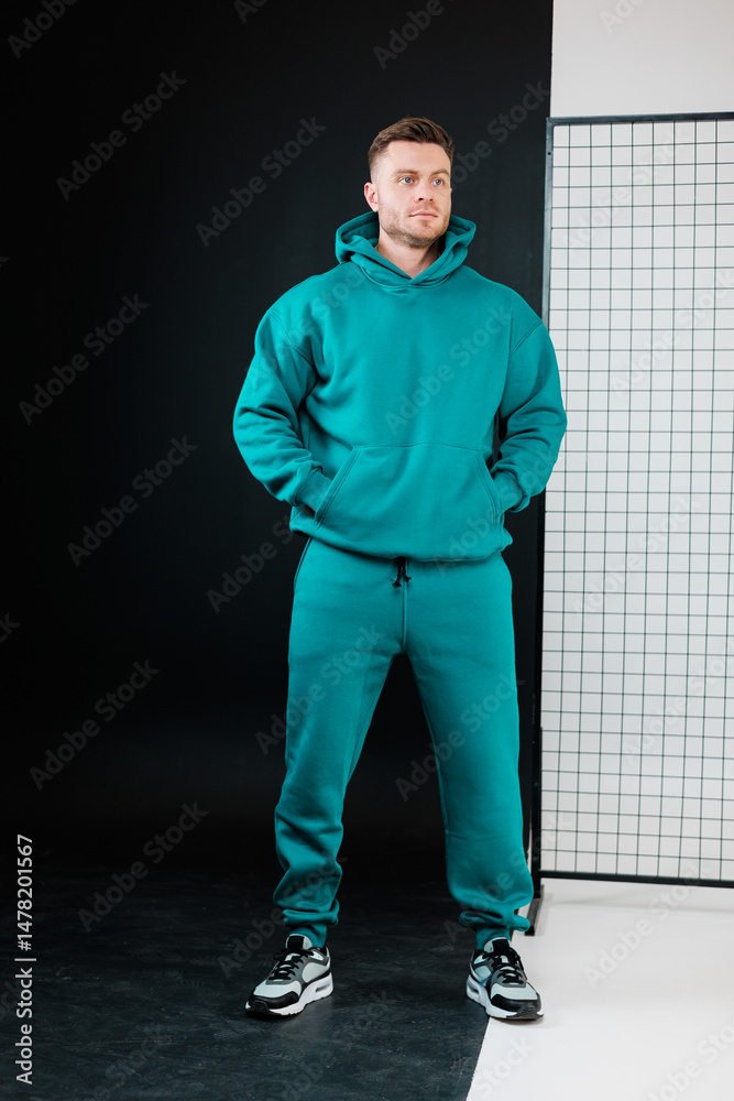 A fashionable male model is showcasing a vibrant teal hoodie paired with stylish joggers, all set against a modern and contemporary background that complements his activewear aesthetic perfectly