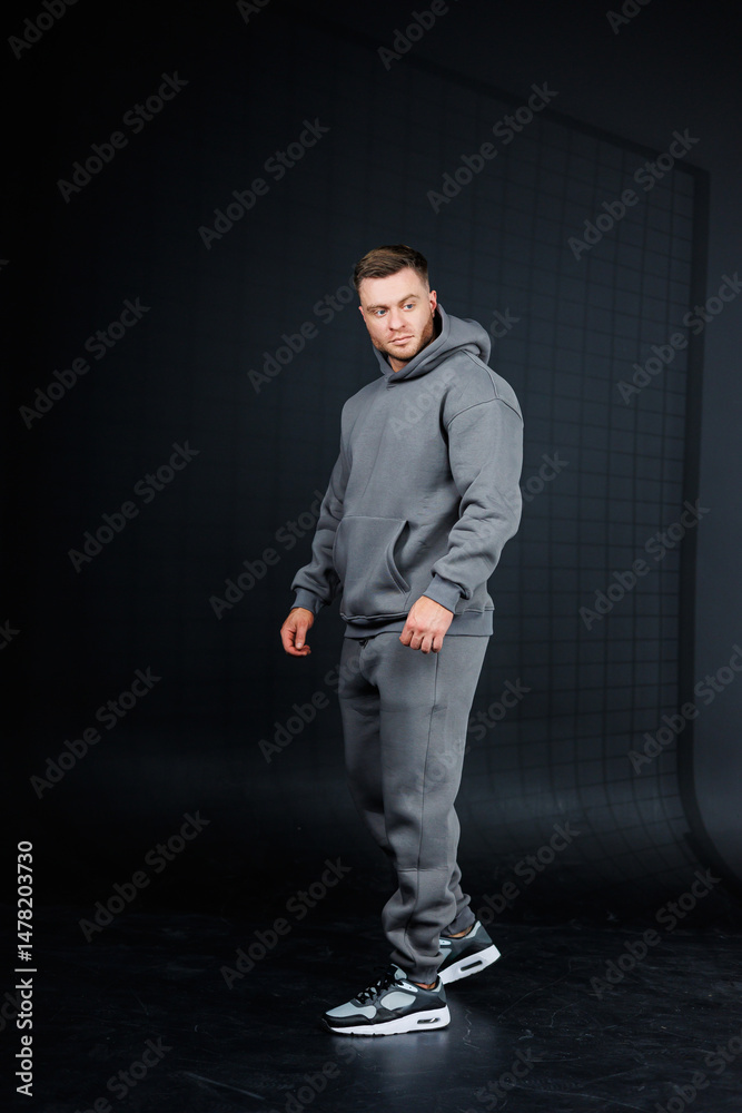 Casual Sportswear Lifestyle A Young Man in a Stylish Grey Hoodie and Comfortable Joggers Posed against a Dark Background, Representing a Trendy and Sporty Fashion Statement for Active Individuals