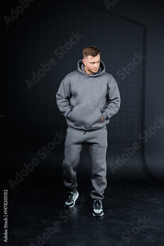 Obraz na płótnie A fashionable young man wearing a modern gray hoodie and matching sweatpants, perfect for showcasing an urban fashion collection that highlights the latest trends in activewear apparel w salonie