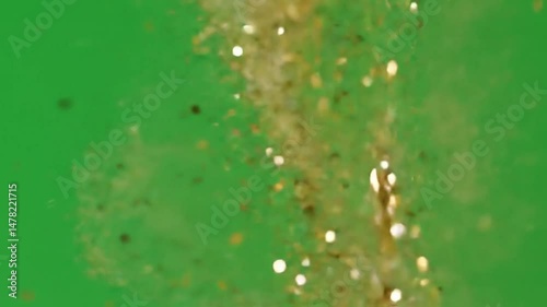 Gold glitter falling against a vibrant green screen for visual effects use