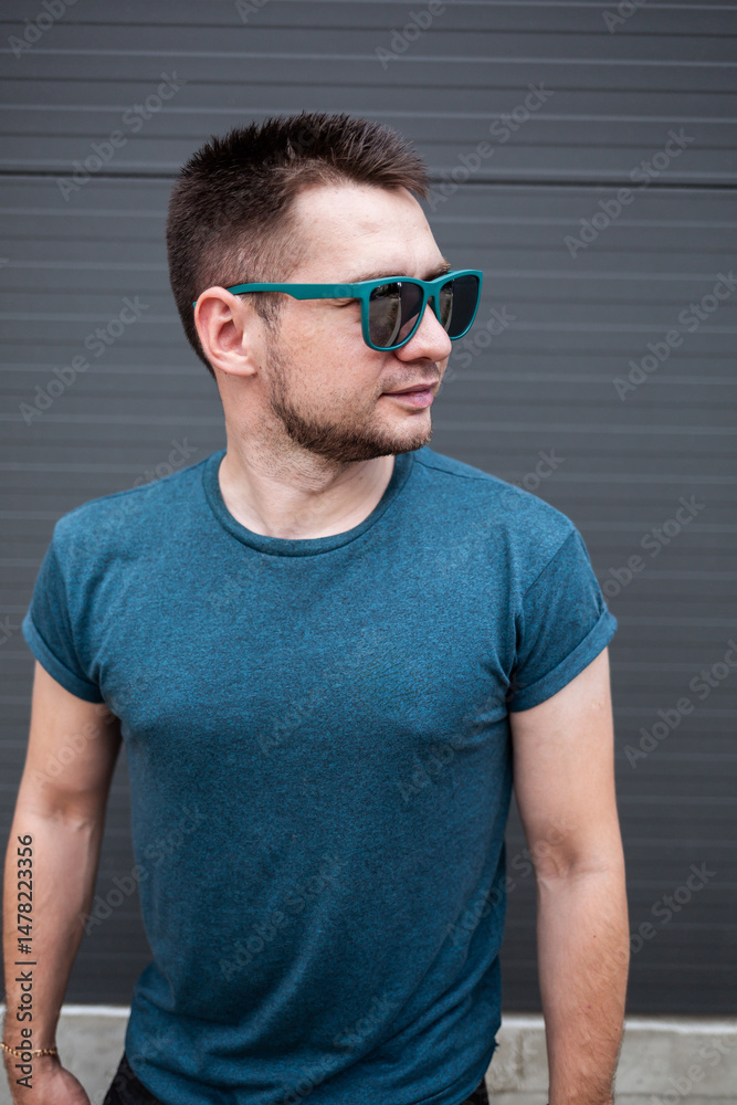 A stylish young man in a trendy blue Tshirt and sunglasses strikes a confident pose against a sleek, modern architectural backdrop, reflecting todays contemporary urban lifestyle