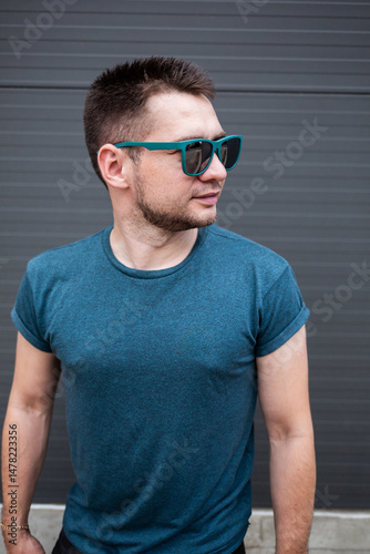 Obraz na płótnie A stylish young man in a trendy blue Tshirt and sunglasses strikes a confident pose against a sleek, modern architectural backdrop, reflecting todays contemporary urban lifestyle w salonie