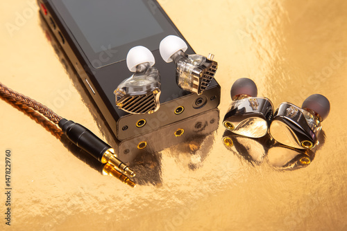 Wired earbuds on a black audio player with a gold backdrop, showcasing a braided cable. Great for technology, sound equipment, and design themes. High-quality image.