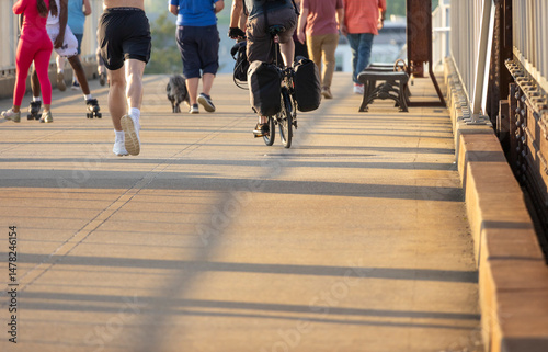 People walking, jogging, rollerblading, and bike riding on a sidewalk on a summer evening. 