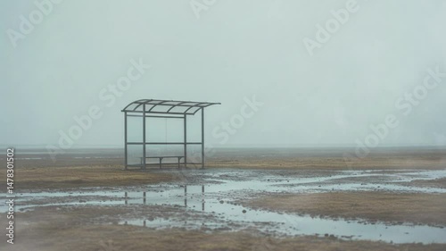 Abandoned bus stop shelter in foggy landscape with puddles  