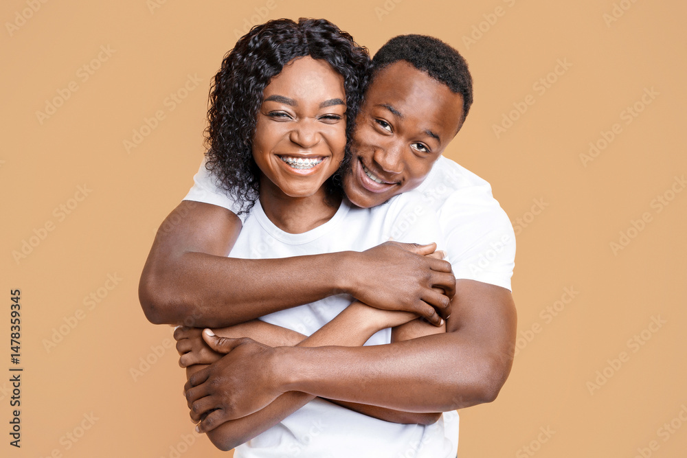 Obraz premium Loving black couple cuddling over yellow studio background. Cheerful young african american man and woman hugging and smiling at camera. Love, relationships, marriage concept