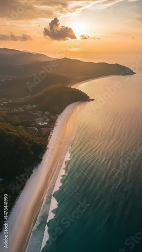 Coastal Sunset Aerial: Golden hour illuminates a pristine beach curving along a tranquil ocean, nestled between lush green hills under a vibrant sunset sky.