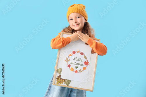 Cute little happy girl holding frame with autumn painting on blue background