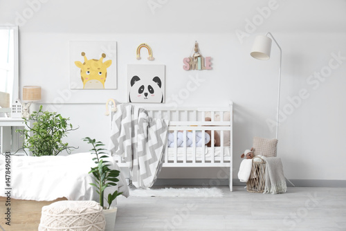 Stylish white crib with plaid and pictures on wall in interior of light children's room