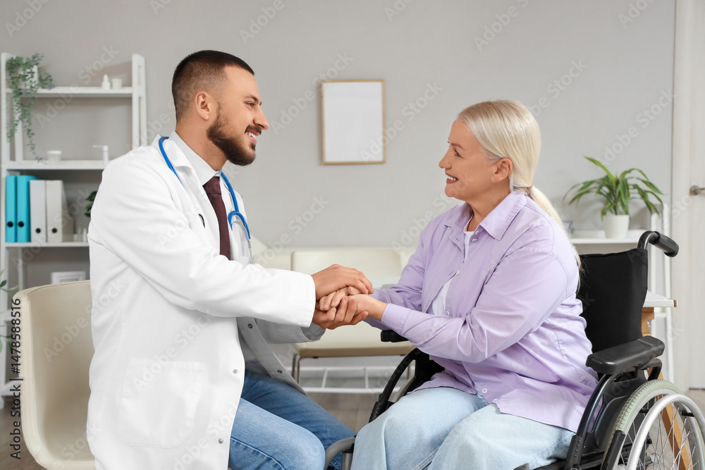 Obraz premium Male doctor with mature woman in wheelchair holding hands at hospital