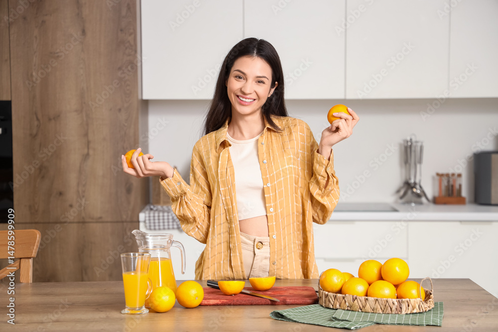Obraz premium Young woman with fresh oranges and juice in kitchen