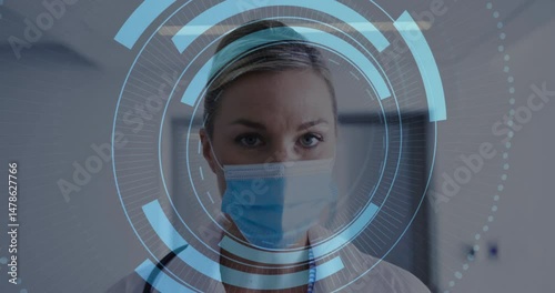 Female doctor scanning data on digital HUD overlay in hospital corridor wearing mask and lab coat