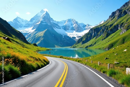 Scenic winding road journey through vibrant green alpine meadows alongside a pristine mountain lake, majestic snow-capped peaks reflecting in tranquil blue water