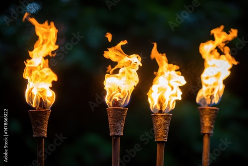 Four tiki torches burning brightly at night in a tropical garden setting close up shot with blurred background