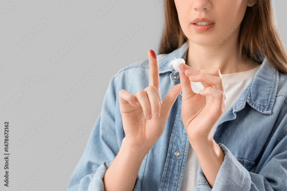 Young woman with injured finger and medical wool on grey background Young woman with injured finger and medical wool on grey background