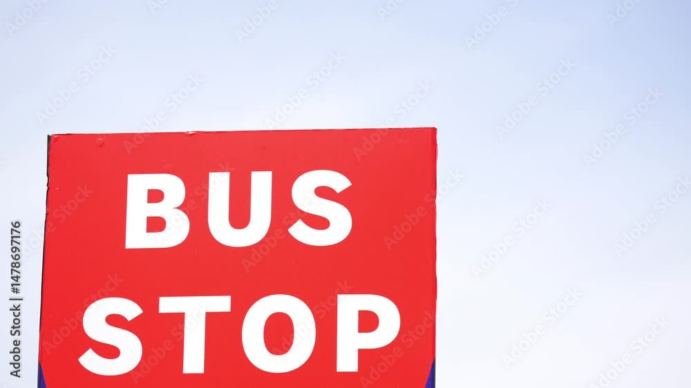 Bright red bus stop sign against clear sky in urban area